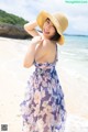 A woman in a dress and hat on the beach.