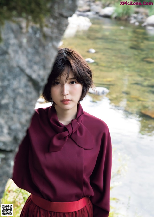 A woman in a red dress standing by a river.