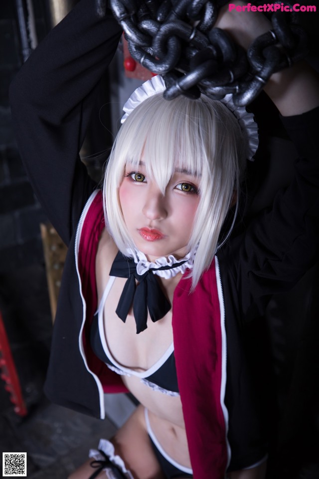 A woman in a maid outfit holding a chain around her neck.