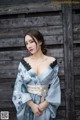 A woman in a blue kimono posing in front of a wooden wall.