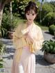 A woman in a yellow kimono standing next to a tree.